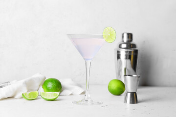 Glass of tasty margarita cocktail, shaker and limes on light background