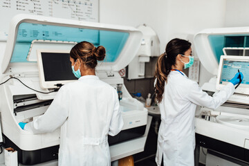 Fototapeta premium Two female scientists or technicians with face protective masks work in laboratory on human blood samples.