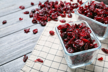 Bowls with tasty dried cranberries on color wooden background, closeup