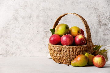 Basket with ripe pears and apples on light background