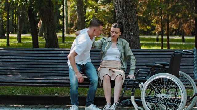 A guy transfers woman from a wheelchair to bench