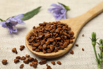 Wooden spoon of chicory granules on sackcloth, closeup