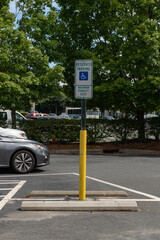 Blue and white Handicap parking sign on a yellow pole in a parking lot with a shallow depth of field