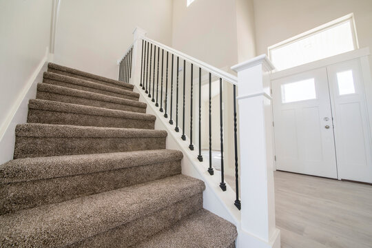 Carpeted staircase with white newel post inside a house with white siding
