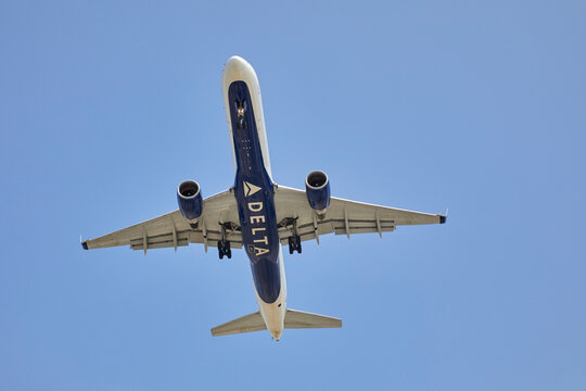 A large airplane putting landing gear down flying overhead with a blue sky in the background
