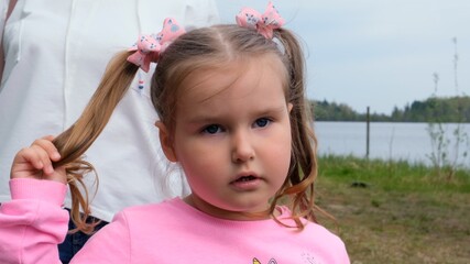 Portrait of a cute 3 year old girl, dressed in a pink sweatshirt with two ponytails, playing outdoors in nature. Happy childhood concept, children development