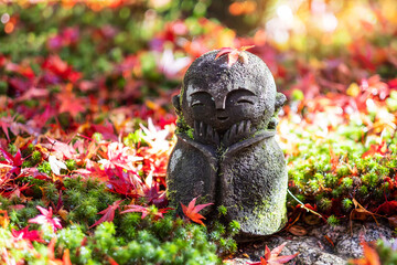 Japanese Jizo sculpture doll with falling Red Maple leaf in Japanese Garden. Landmark and famous in...