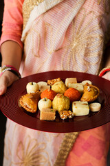 Indian woman serve Diwali sweets Gujiya peda barfi Indian Sweet dessert mithai festival dish...