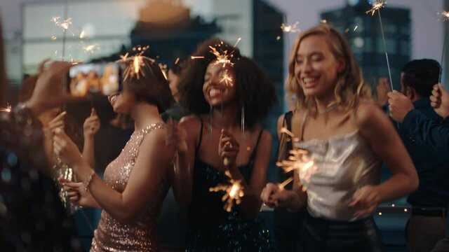 beautiful young women dancing with sparklers girl friends celebrating new years eve at glamorous party wearing stylish fashion friend using smartphone sharing video of celebration on social media