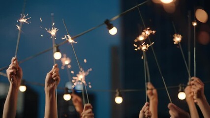 close up hands holding sparklers group of friends celebrating waving sparkler fireworks dancing enjoying new years eve party having fun holiday celebration at evening social gathering on rooftop 4k