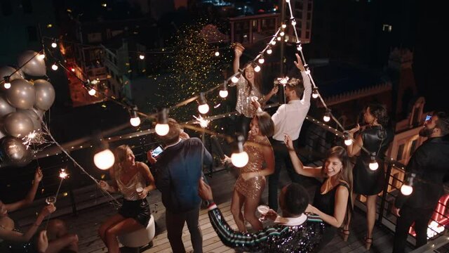 top view friends celebrating new years eve party dancing throwing confetti enjoying glamorous celebration wearing stylish fashion social gathering on rooftop at night 4k 