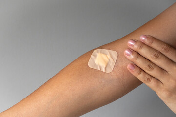 Close up of female hand with a band-aid glued, gray background with copy space. Blood donor concept.