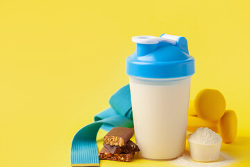 Protein sport shake, bars, dumbbells and powder on yellow background . Fitness food and drink. Diet