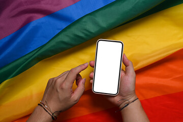 Man holding smart phone with blank screen over colorful rainbow flag. LGBT.