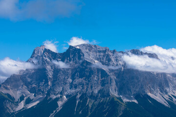 Zugspitze mountain massif disappearing in fog and clouds with dramatic sky. Copy space. Template for travel and tourism concept.