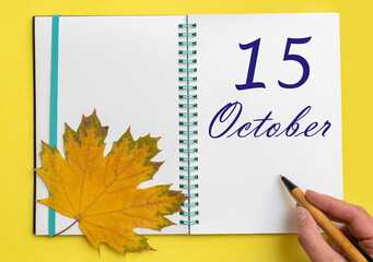 Hand writing the date 15 october in an open notebook with a beautiful natural maple leaf on a...