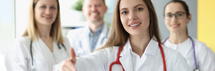 Woman doctor stretching out her hand for handshake on background of colleagues
