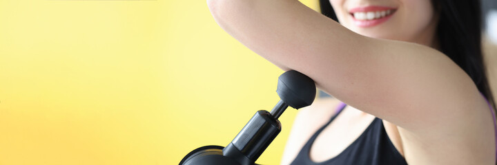 Young woman doing shoulder muscle massage with percussion massager closeup