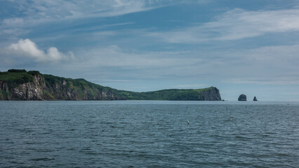 The coastline of Kamchatka. Picturesque cliffs with steep slopes and green vegetation against the blue sky. Ripples on the surface of the Pacific Ocean.  Petropavlovsk-Kamchatsky.  Avacha Bay
