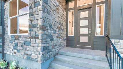 Pano Home facade with stone brick wall and gray front door with frosted glass panels