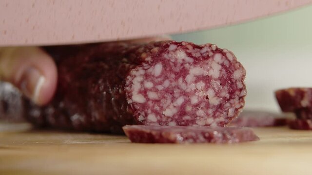 Sausage slicing, Close view woman hand's cutting sausage with sharp knife. Hand slicing salami sausage on wooden chopping board. Footage of slicing smoked pork