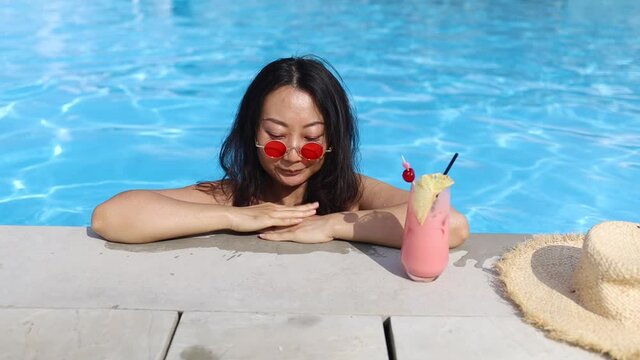 beautiful young asian woman with cocktail relax around outdoor swimming pool in hotel resort 