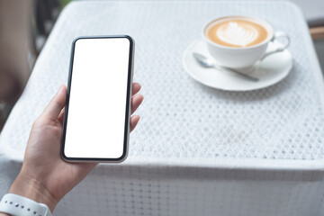 Cell phone mockup image blank white screen.  Woman hand holding, using mobile phone at coffee shop.