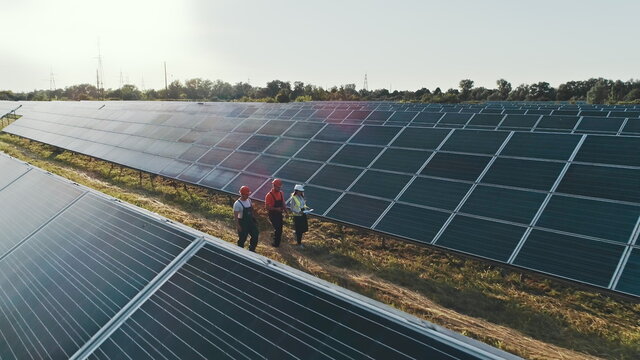 Top view of specialists walking across a solar power plant. Three employees of alternative power plant walking and talking about scheme of solar panels.