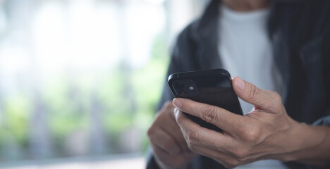 Close up of man in casual wear hands holding, using mobile phone, chatting via mobile apps with blurred background