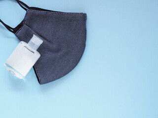 Top view, Dark blue fabric face mask and alcohol gel in bottle to prevention pollution and viruses on blue background. Healthcare, Medical and New normal concept. Copy space for your text..