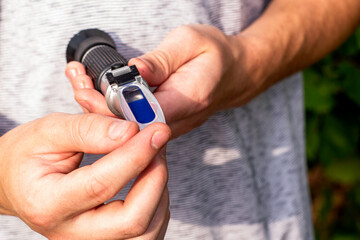 the grower holds a refractometer in his hands to determine the amount of sugar in grape juice