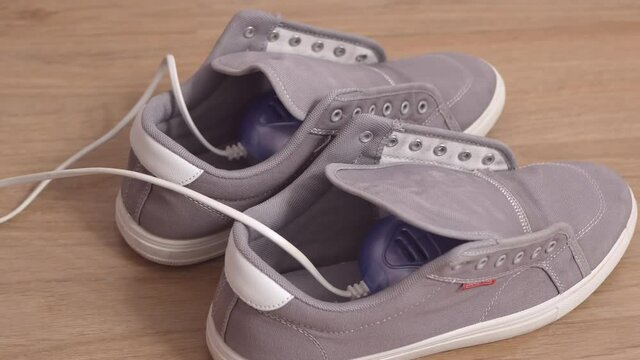 Woman puts shoe dryer in wet grey gumshoes. Drying of wet grey gumshoes.
