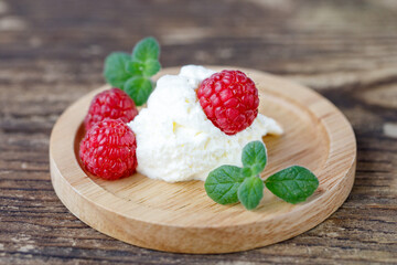 wooden plate of whipped cream with raspberries and mint leaves close-up on dark brown wooden background.