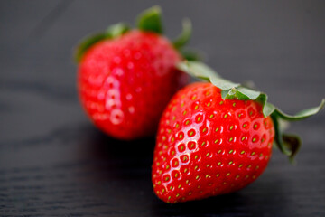 close up and side view of two large fresh red sweet strawberries on wooden black background, horizontal, copy space.