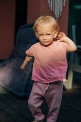 Portrait of smiling little girl standing by house. Adorable toddler wearing pink clothes looking at camera and smiling. Childhood concept