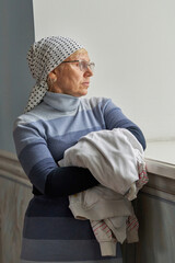 Fototapeta premium woman in glasses with a scarf on her head is leaning against windowsill
