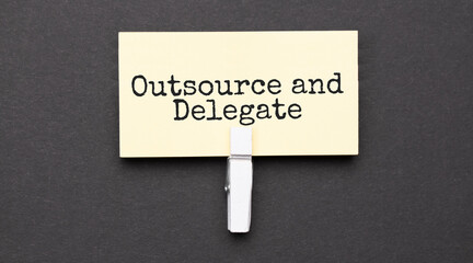 outsource and delegate text on paper with wihte clip. On black background
