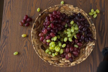 a fruit basket with full of green and red grapes, a wine bottle, a goblet on a woodden table 2