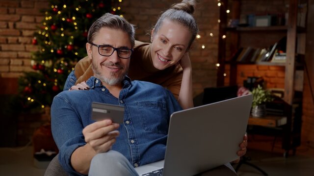 Couple buying Christmas gifts online from home with laptop and credit card.