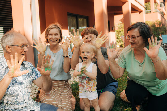 Portrait of happy multi generation family posing with their hands dirty in paint. Mid adult parents, grandparents and toddler girl smiling at camera outdoors. Creative family concept