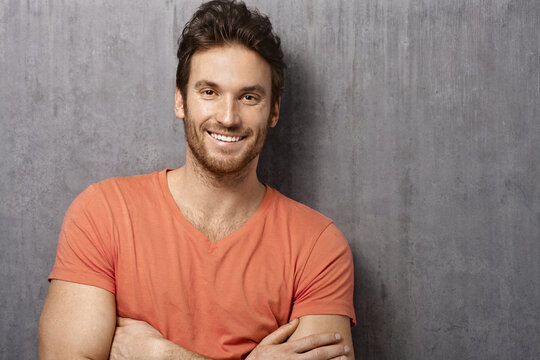 Portrait of happy white young man smiling, standing against white concrete wall. Copy space, casual clothing.