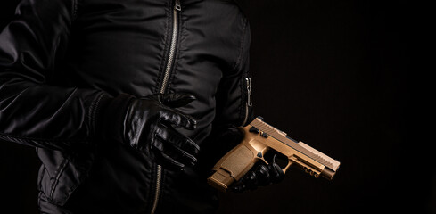 A man in a black jacket and black gloves holding a gun on a dark back
