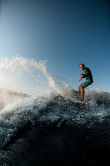 man skilfully riding wave on the wakesurf on the background of blue sky - obrazy, fototapety, plakaty