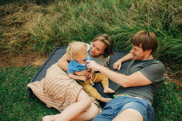 Portrait of happy family resting on grass outdoors. Couple lying on mattress and teasing their...