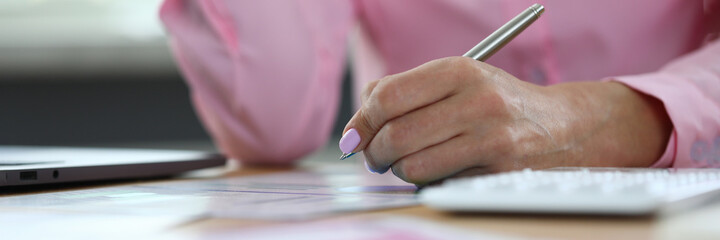 Woman hand holds pen and makes notes in documents at working table