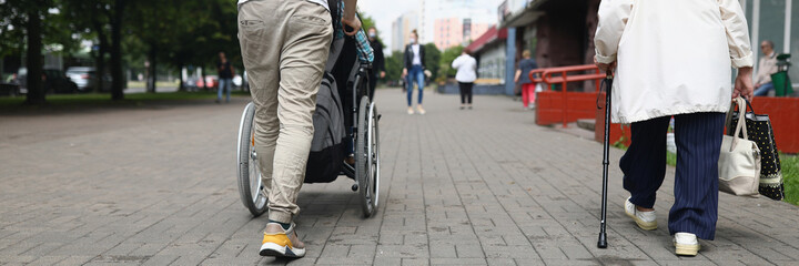 Fototapeta na wymiar Man rolls a seated woman in wheelchair down street in city