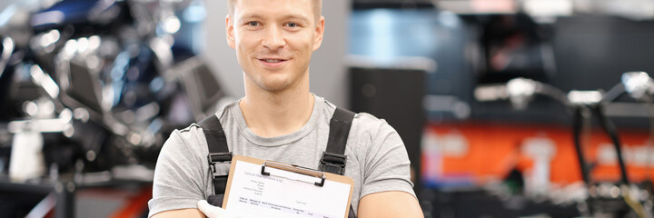 Handsome auto mechanic posing in car service and holding documents in hands