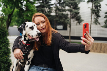 Young reddish woman at the street with her dalmatian dog taking a picture with mobile phone....