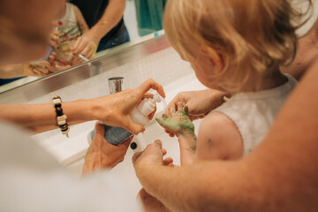 Parents washing hands of little child with soap. Mother squeezing liquid soap on hands of daughter....