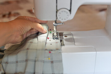 stitching on a sewing machine through tailor's needles, a dressmaker at home sews a silk shirt on a sewing machine.